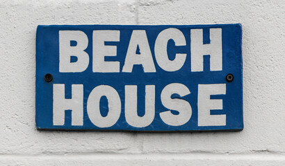 Generic blue and white rustic BEACH HOUSE sign affixed to a wall.
