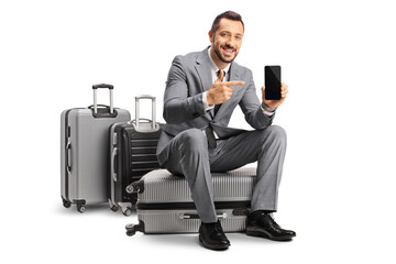 Bussinessman sitting on a suitcase pointing at a smartphone