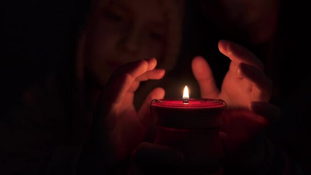 Mom and child are wrapped in a blanket, shivering from the cold on the bed in an unheated apartment and getting hot from a candle. Power outages and central heating due to the energy crisis.	
