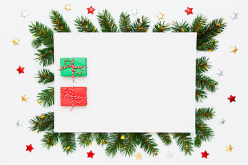 Christmas, New Year holiday layout with copy space. Blank white paper with two small Christmas gifts in frame of natural fir tree branches and decorations on white flat lay background.