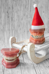 
Lustiger zahnärztlicher Weihnachtshintergrund mit Platzhalter. Zahnmodell mit festsitzender Zahnspange trägt eine Weihnachtsmütze und isst eine Weihnachtskuge - obrazy, fototapety, plakaty