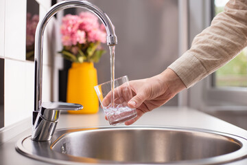 Close up of a man hand filling a glass of water directly from the tap. Filling glass of water from...