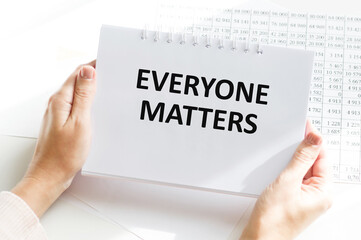 EVERYONE MATTERS text on a notebook in the hands of a person on the background of an office desk