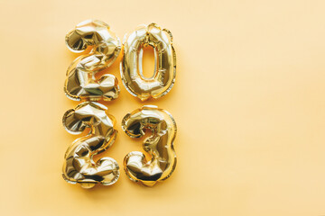 Vertically arranged balloons made of gold foil in the form of the numbers 2023 on a yellow background. Celebrating Christmas, New Year and festive concept. Flat position, top view.