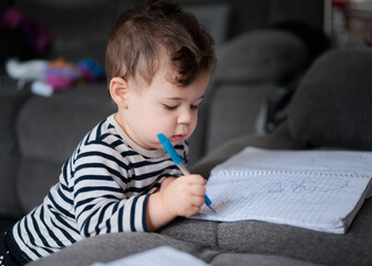cute baby boy writing in a notebook on the couch at home