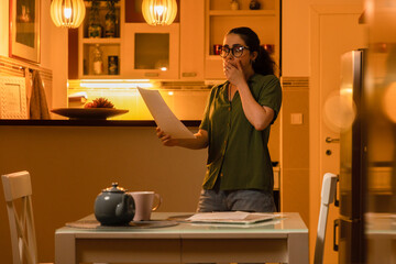 Young frightened shocked Caucasian woman wearing glasses looks at documents while standing in...