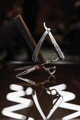 Fototapeta na wymiar Barber shop equipment sets on dark glass background. Comb, steel scissor and vintage straight razor in air. Professional hairdressing tools. Beauty industry, art, self-care concept. Place for text.
