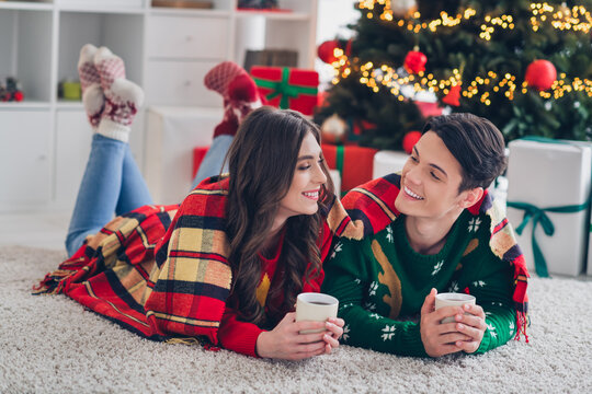 Photo of two chilling positive young wear comfortable warm outfits drink hot home cacao under nice plaid near big adornment christmas tree indoors