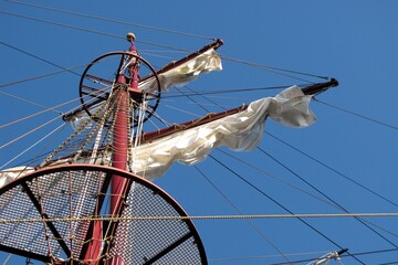 looking up at an old sail boat or pirate ship mast with closed sails and a blue sky