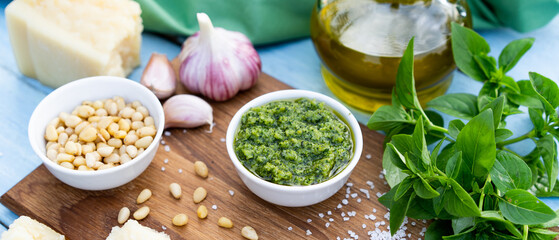 ingredients for the preparation of pesto sauce. basil, pine nuts, garlic, basil, parmesan on a blue table and wooden board, banner