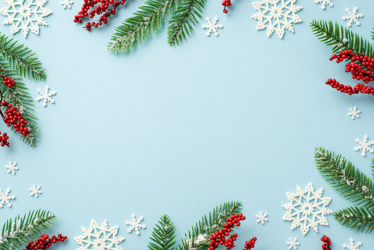 Winter holidays concept. Top view photo of spruce branches in hoarfrost mistletoe berries and snowflake ornaments on isolated pastel blue background with empty space in the middle