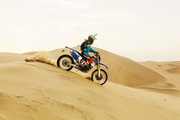 A person on a dirt bike in the Peruvian desert rides across sand dunes