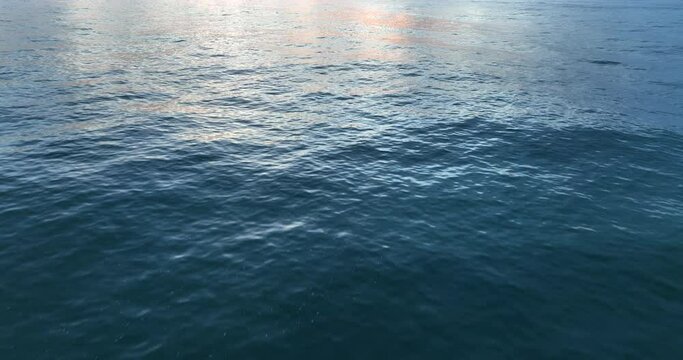 Aerial shot of dusk above ocean surface in sunrise golden hour. Drone flies over the water in slow motion.