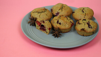 on a gray round plate with a brown star of anise on a pink background of the table are several gluten - free chocolate muffins with cherries . side view . diet cupcake made at home