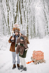 Young family with two children standing in winter forest and posing for a photo