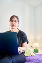 Vertical shot of Caucasian pensive woman looking at computer from bedroom