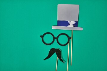 Hat, glasses and mustache on sticks for a photoshoot, party celebration items on green background