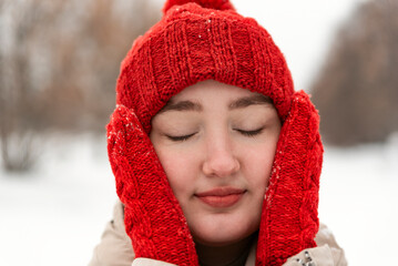 Fashionable red knitted hat and mittens on beautiful girl. Close-up face of woman in knitted headdress in outside