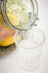 A stream of lemonade from a bottle of liqueur from elderberry flowers pouring into a faceted glass. Medicine with elderberry flowers. A cool refreshing summer drink