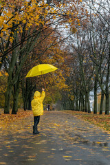 Child walks in rain in park with an umbrella in hands. Vertical frame