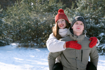 Cheerful young couple in winter in forest. Guy rolls the girl on his back.