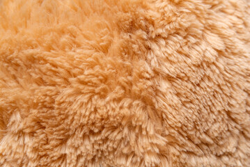Close-up crumpled faux fur in peach or beige hue. Structure of fur fabric as background. Top view