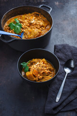 Traditional Indian vegetarian Madras curry stew with sweet potatoes and roasted cashew nuts served as close-up in design bowl and saucepan
