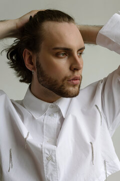 Bearded guy holds his curly hair in a  stylish white shirt looks away