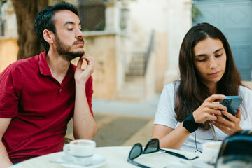Young couple sitting in a cafe terrace checking smartphone