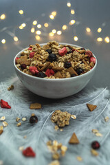 A bowl of muesli on a gray monochrome background, with white feathers and a side from a garland. Healthy food, healthy breakfast
