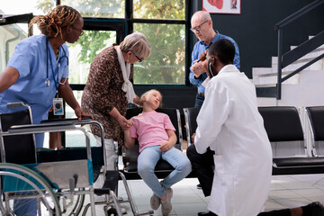 Little girl faints and collapses on the chair in hospital waiting area during medical consultation, scared grandparents trying to help. Practitioner doctor consulting child trying to wake up her