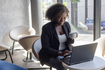 successful smiling business woman in cafe works on laptop computer