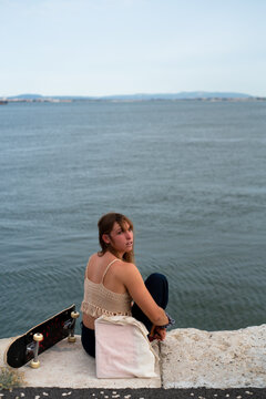 Young woman sitting by the river with skateboard