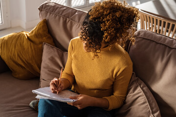 Freelancer sitting on couch and writing in notepad
