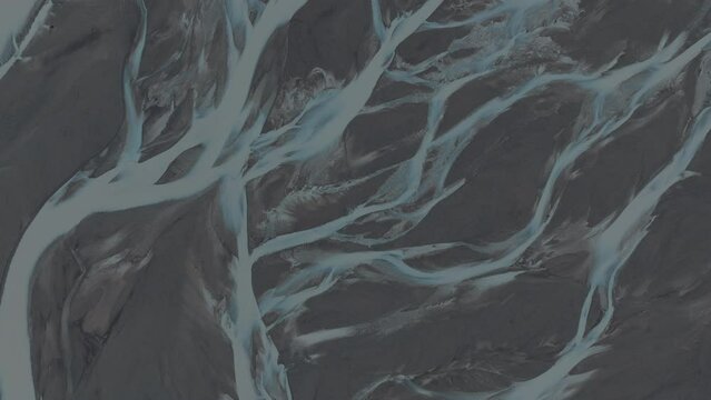 Amazing topdown close-up shot of clear blue river streams breaking up the dark volcanic landscape. Forces of the nature are creating surreal glacial river pattern. 
