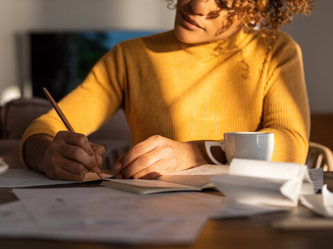 Crop businesswoman making notes near notepad and cup