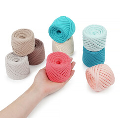 Spools of multi-colored cotton threads on a white background. Cotton yarn in ball and bobbins. Woman's hand holding one roll.