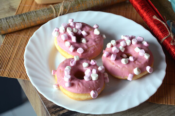 Three donuts with pink icing on a plate on a wooden table. Sweet breakfast.