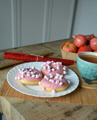 Cup of black tea with lemon and three donuts with pink icing on a plate on a wooden table. Sweet breakfast.