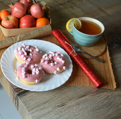 Cup of black tea with lemon and three donuts with pink icing on a plate on a wooden table. Sweet breakfast.