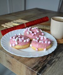 Cup of black tea with lemon and three donuts with pink icing on a plate on a wooden table. Sweet breakfast.