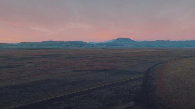 Breathtaking pink sunset behind the endless volcanic gravel landscape. Small rural villages below the majestic mountains. Incredible Iceland, perfect tourist destination. Aerial bird's eye shot. 