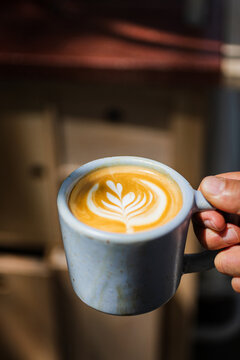Hand holding a clay cup with coffee art latte 