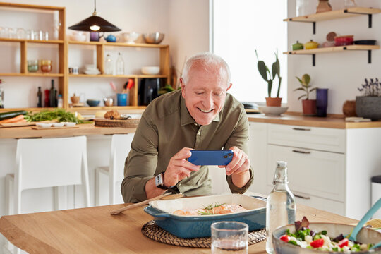 Elderly man taking photo of food in kitchen