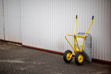 a yellow wheelbarrow stands by the wall