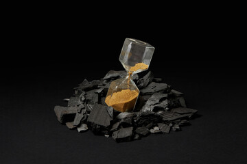 Sandglass with golden sand pile of coal.