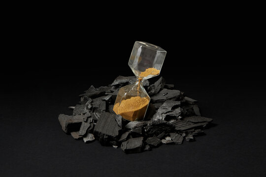 Sandglass with golden sand pile of coal.