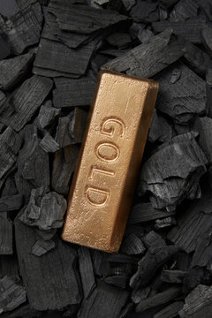 Gold ingot laid on coal pieces, close up.