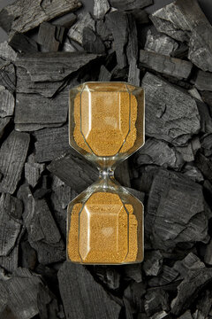 Hourglass with golden sand on pile of black coal.