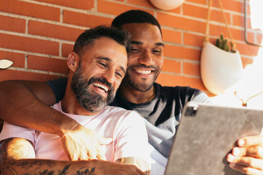 Smiling multiracial gay couple making video call with tablet